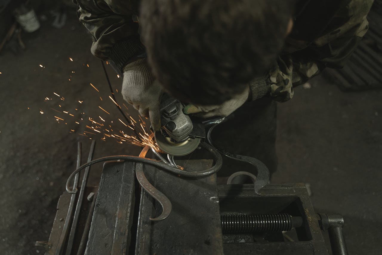Close-up of a blacksmith using an angle grinder on metal, producing sparks in a workshop setting.