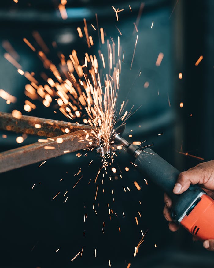 Close-up of a workers hand operating a grinder, sending bright sparks against a dark background in an industrial setting.