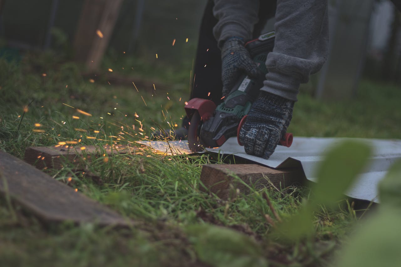Close-up of a person using an angle grinder on metal outdoors, with sparks flying.