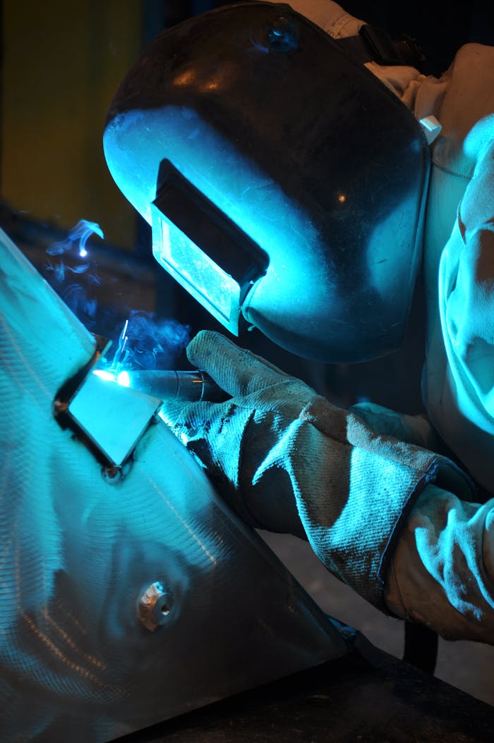 A skilled welder in protective gear working on metal in an industrial environment.